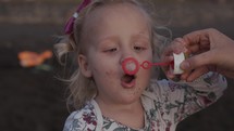 A slowmotion of an adorable little girl who is blowing soap bubbles