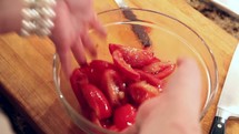 A woman mixing tomatoes in a bowl with her hands.