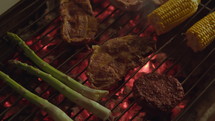 Corn, chicken, beef, and asparagus cooking on a hot charcoal grill