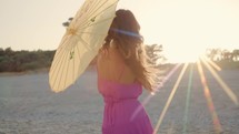Fashion Model Girl On The Beach with umbrella at sunset time