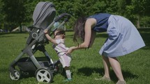 a mother and toddler girl pushing a stroller through the grass