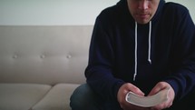 a man sitting on a couch holding a Bible and praying 
