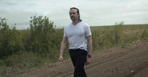 Young man walking on unpaved, dirt road on summer day explore, hiking, worshipping and praying. Lifestyle, worship and prayer concept.