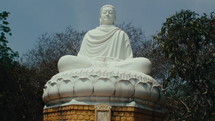 Panorama of a large Buddha statue sitting, surrounded by trees. Tilt up shot