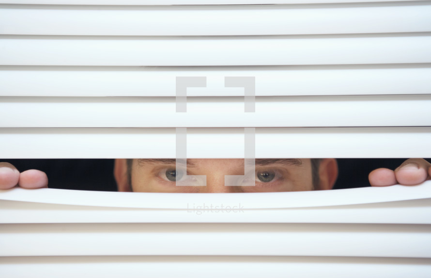 Caucasian man looking through the slats of a blind
