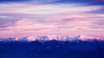 Snow-covered white mountain peaks, pink clouds at dusk, timelapse