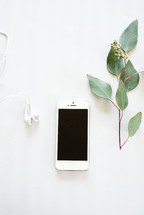 Earphones, a cell phone, and a sprig of green leaves on a white background.