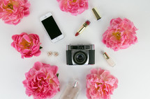pink flowers, camera, lipstick, perfume, cellphone, earrings on white background 