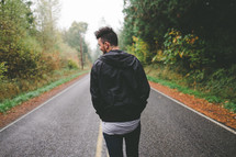 A man walking down an empty highway through the woods.