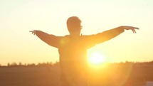 a man standing in a field at sunset with raised hands 