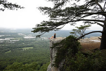 a woman sitting on the edge of a cliff 