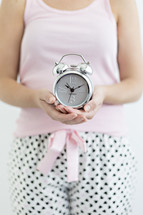 a woman in pjs holding an alarm clock 