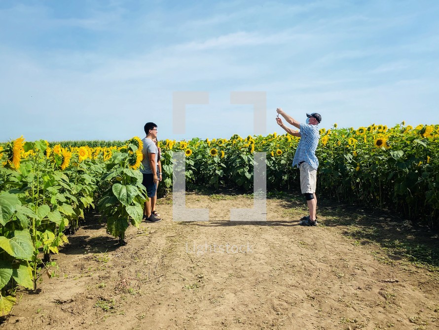 a man taking a picture of a couple standing near a field of sunflowers 