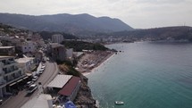 Aerial of Himare, Albania's coastal road, crystal-clear sea, and majestic mountains.