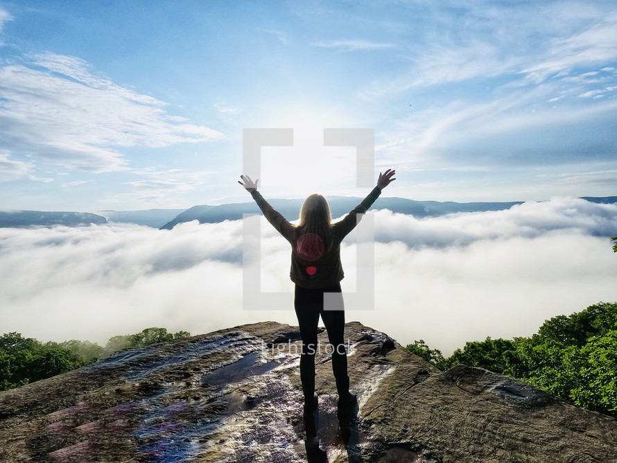 a woman standing on a mountaintop with hands raised 