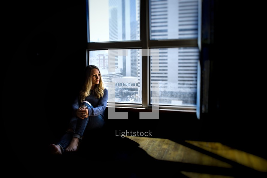 woman sitting on a floor next to a window in a city 