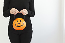 a person holding a jack-o-lantern candy bucket 