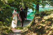 a bride and groom walking holding hands on a path 