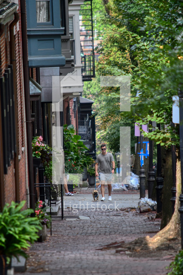 a man walking his dog on a narrow cobblestone street in Boston 