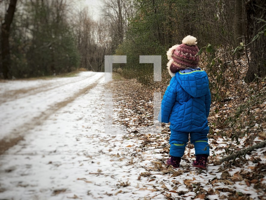 toddler standing on a snow covered dirt road 