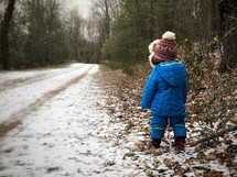 toddler standing on a snow covered dirt road 