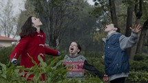 Three young kids standing enjoying the pouring rain in slow motion