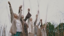 women walking through a field of tall grasses with raised hands 