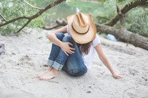 woman in cowboy hat sitting on a beach 