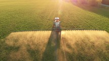 Aerial footage. Pesticide Sprayer Tractor working on a large green field at sunset. Aerial shot following on the side a tractor spraying wheat field against diseases. Farmer spraying soybean fields.