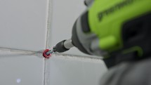 Electric screwdriver driving a screw into a tile wall in slow motion