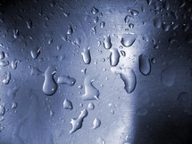 Beads of water droplets on a glass surface where condensation has built up from the cold weather outside of a window of a warm house. 
