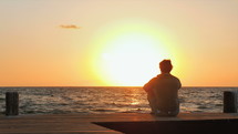 a man sitting on a dock at sunset 