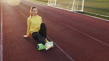 Rehabilitation medicine. Sport woman using roller stick for massage in sport arena. Female athlete uses a massage foam roller sitting on a stadium. Workout to remove pain. Fitness outdoors concept.