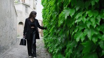 Woman Dressed In Black Walks Touching Ivy In A City Alley Of Gerace