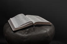 An open Bible on a leather stool.