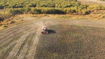Aerial shot of a moving combine harvester collecting sunflower seeds in autumn. Agriculture food production. Combine harvesting, collects ripe sunflower grains. Harvest, Drone, Eco.