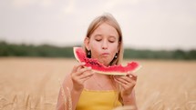 Girl eating juicy watermelon standing in wheat field on sunny summer day. 