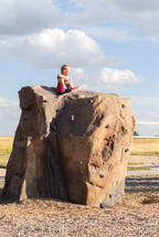 a boy child sitting on a rock outdoors 
