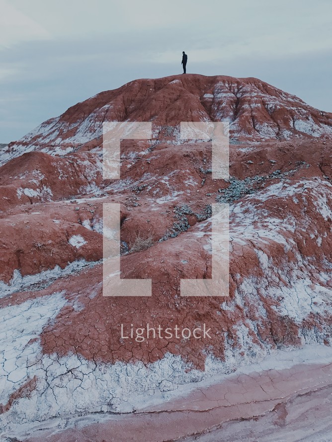 a man standing at the top of a red rock peak 