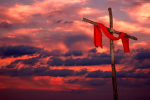 red tunic hanging on a wood cross against a fiery sky at sunset 