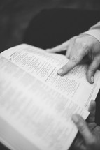 Hand pointing to scripture in open Bible.