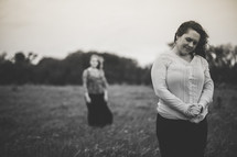 Mother praing in a field, with daughter standing in the background.