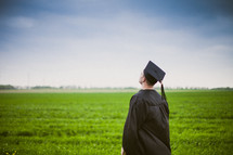Graduate standing in a field of greeen grass looking up.
