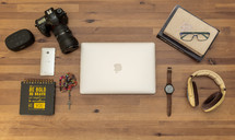Laptop, DSLR, phone, headphones, Catechism, Bible, Notepad, Glasses, Watch and Rosary on a Desk