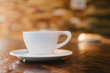 A white cup and saucer on a wooden table.