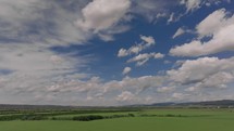 Aerial drone slowly advances over green landscape with beautiful clouds