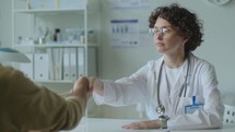 Young Female Doctor Shaking Hands with Patient on Medical Consultation
