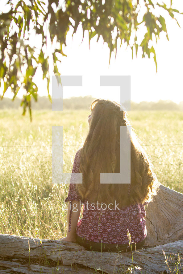 teen girl sitting alone outdoors in a field 