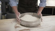 Hands holding sieve and sifting flour at the kithen. Close up, indoor, slow motion.