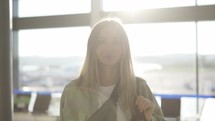 Portrait of a stylish young blonde girl traveller stands in airport terminal in sun light.